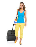 Smiling young tourist woman with wheel bag going straight