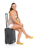 Happy young tourist woman sitting on wheel bag