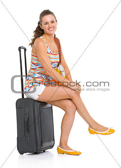 Happy young tourist woman sitting on wheel bag