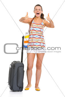 Happy young tourist woman with wheel bag showing thumbs up