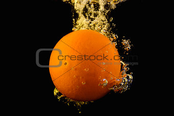 Bright ripe orange dropping into water as it breaks the surface