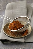 cocoa powder in a metal sieve with a gray background