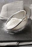 powdered sugar in a metal strainer on a gray background