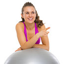 Smiling fitness young woman with fitness ball pointing on copy s