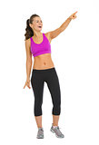 Full length portrait of smiling fitness young woman pointing on 