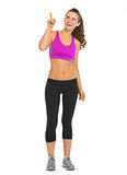 Full length portrait of happy fitness young woman pointing on co