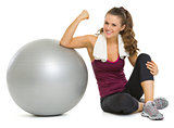 Smiling fitness young woman sitting near fitness ball and showin