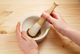 Two hands holding a pestle and mortar with whole coriander seeds