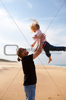 Father throwing daughter in the air at the beach