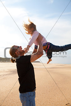 Father throwing daughter in the air at the beach