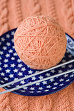 One ball of pink yarn and knitting needles on a blue plate with stars
