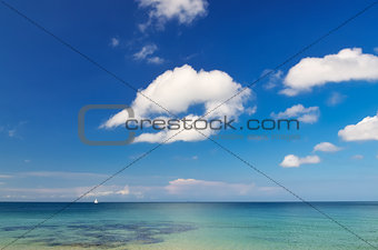 Ocean landscape with blue cloudy sky and little sailboat