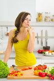 Happy young housewife tasting vegetables while cutting
