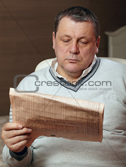 Portrait of senior man reading newspaper at home.