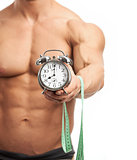 Cropped view of a muscular young man holding clock and measuring tape. It is high time for workout concept.
