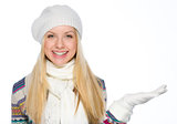 Smiling girl in winter clothes presenting something on empty han