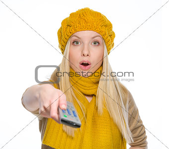 Surprised girl in autumn clothes using tv remote control