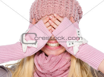 Portrait of happy girl in winter clothes covering eyes with hand