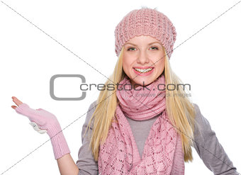 Smiling girl in winter clothes presenting something on empty pal