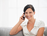Smiling young woman sitting on couch and talking cell phone
