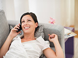 Happy young woman laying on couch and talking mobile phone