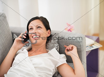 Happy young woman laying on couch and talking mobile phone