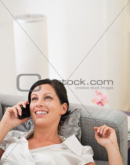 Happy young woman laying on divan and talking cell phone