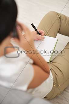 Young woman talking cell phone and writing in notepad. rear view