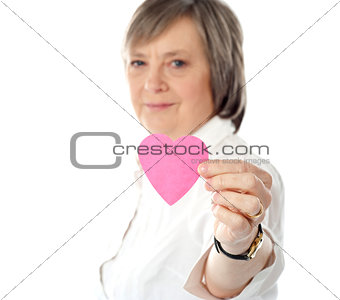 Focus on pink paper heart. Aged woman holding it