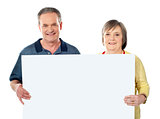 Smiling aged couple holding blank white poster