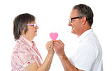 Aged couple holding paper heart. Smiling at each other