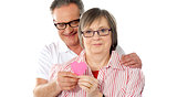 Old couple facing camera with focus on paper heart