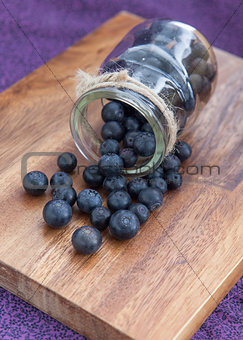 Blueberries poured from a glass jar on a wooden board on a purple background