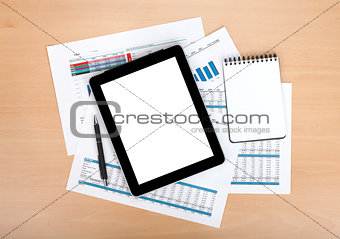 Tablet with blank screen over papers with numbers and charts
