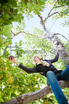 Girl sitting on a apple tree reaching for a branch with apples 
