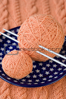 Two balls of pink yarn and knitting needles on a blue plate