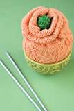 A ball of orange yarn to knit a flower on a green background