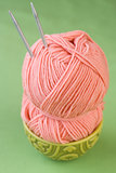 Large pink skein of thread in a plate with oriental ornament national and knitting needles on a green background