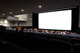 Cinema auditorium with people in chairs watching movie.