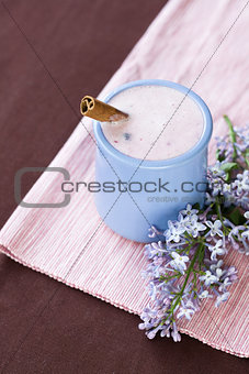 Homemade yogurt with berries in a ceramic bowl on a pink tablecloth, cinnamon stick and a sprig of lilac