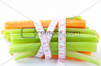 carrots, green celery,  measuring tape on a white background