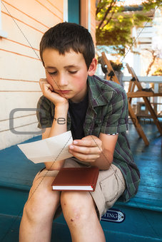 young boy reading letter on front porch