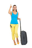 Happy young tourist woman with wheel bag pointing on copy space