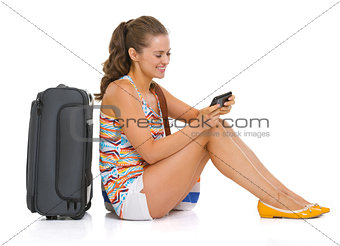 Young tourist woman with wheel bag sitting on floor and writing 