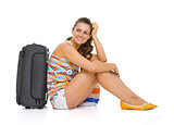Young tourist woman with wheel bag sitting on floor and looking 