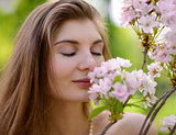 Young Beautiful Woman Smelling a Pink Sakura Flowers