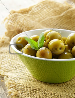 green  marinated olives with herbs  on a wooden table