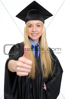 Closeup on smiling young woman in graduation gown showing thumbs