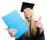 Smiling young woman in graduation gown pointing on book