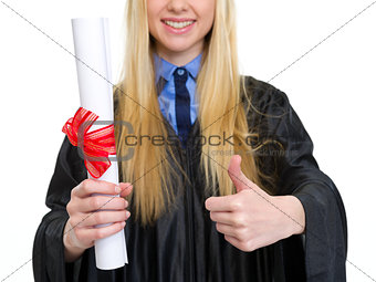 Closeup on young woman in graduation gown showing diploma and th